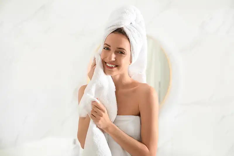 Donna che tampona delicatamente i capelli bagnati con un panno in microfibra per evitare il crespo e la rottura delle cuticole.